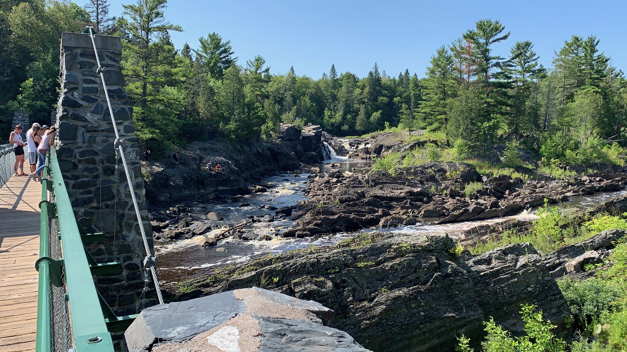 A footbridge crossing the rocky river gorge at Jay Cooke State Park, Minnesota, with people walking across to the far side